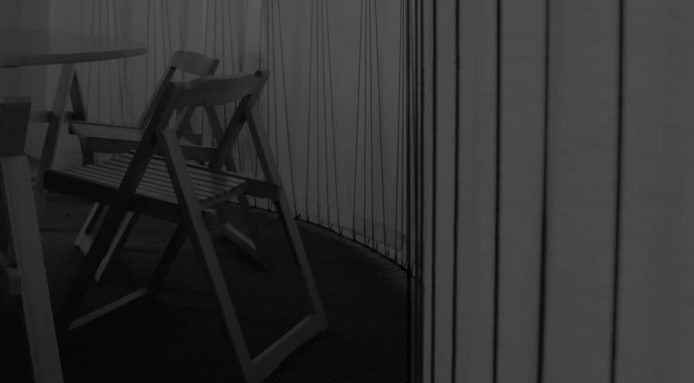 Wooden folding chairs at a round table inside a room walled with taut vertical threads, designed by Figments Experience Lab